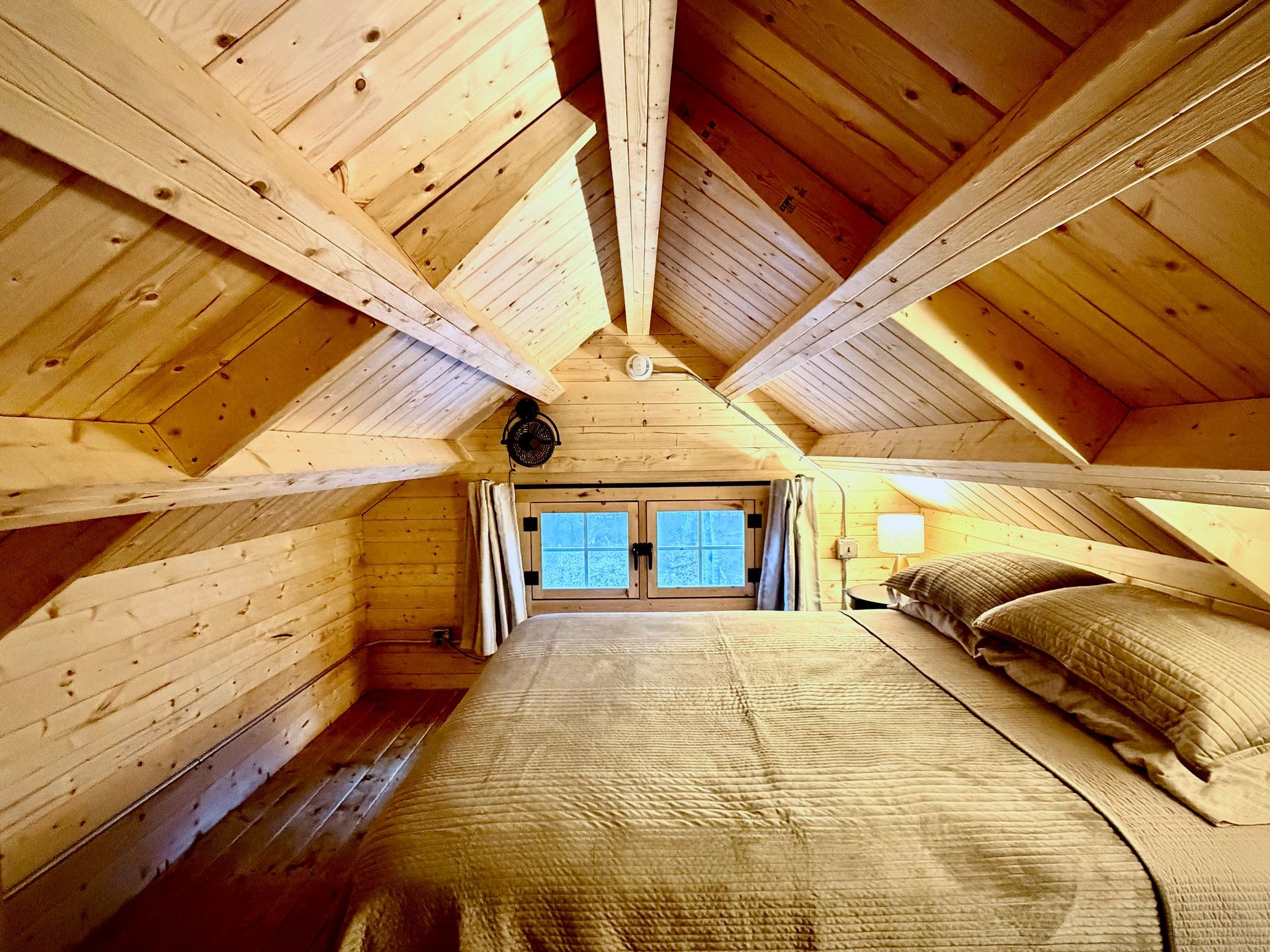 Wooden loft bedroom with sloped beams, bed, and blue window views