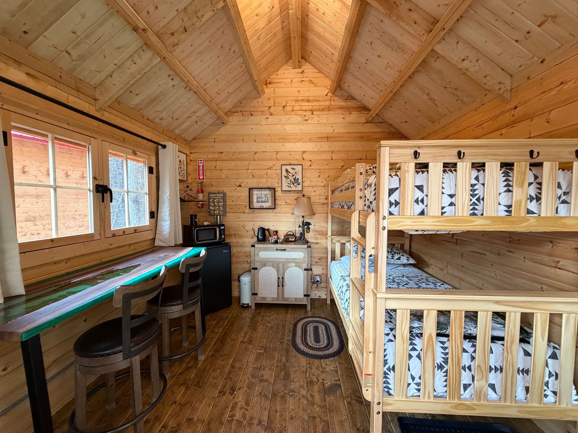Wooden cabin loft with bunk beds, desk, and windows under a vaulted ceiling