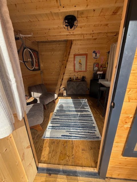 Small wooden cabin room with a striped rug, chairs, and a desk under a slanted ceiling.