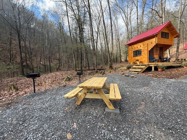 Picnic table on gravel beside a small orange cabin with a red roof in a wooded clearing