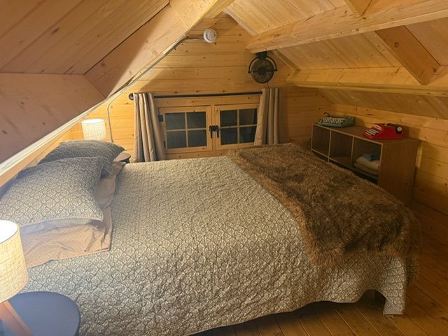 Cozy attic bedroom with a bed, lamp, and small window under a wooden sloped ceiling