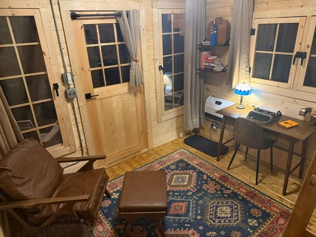 Cozy cabin room with wooden doors, leather chair, patterned rug, desk lamp, and small desk.