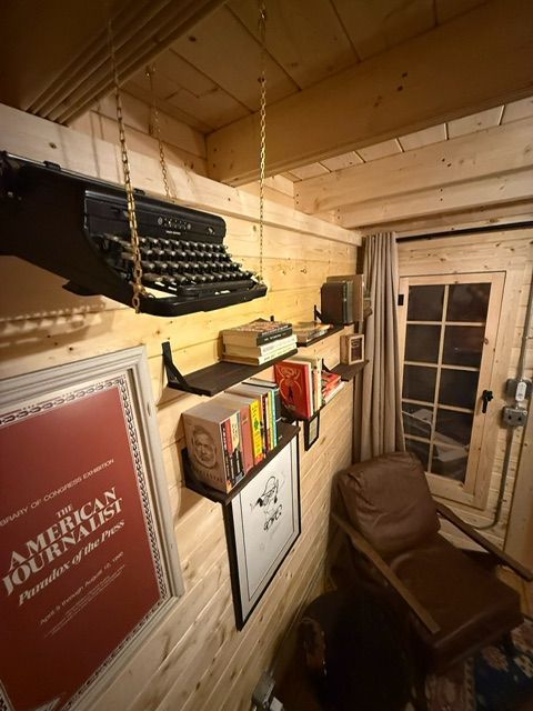 Cozy wood-paneled room with a typewriter shelf, framed poster, chair, and curtained glass door