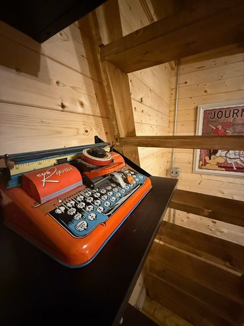 Orange vintage typewriter on a shelf in a wooden room with exposed beams