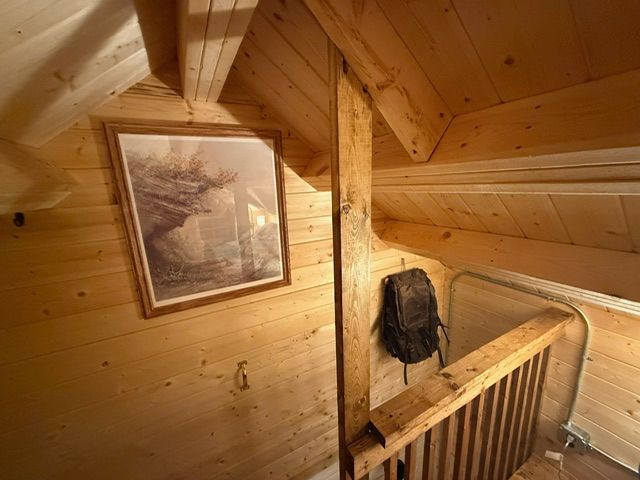 Wooden attic room with slanted walls, a framed painting, and a staircase railing.