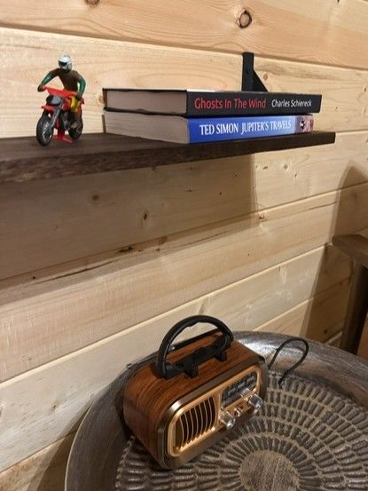 Small toy figure on a wooden shelf beside stacked books and a vintage radio speaker