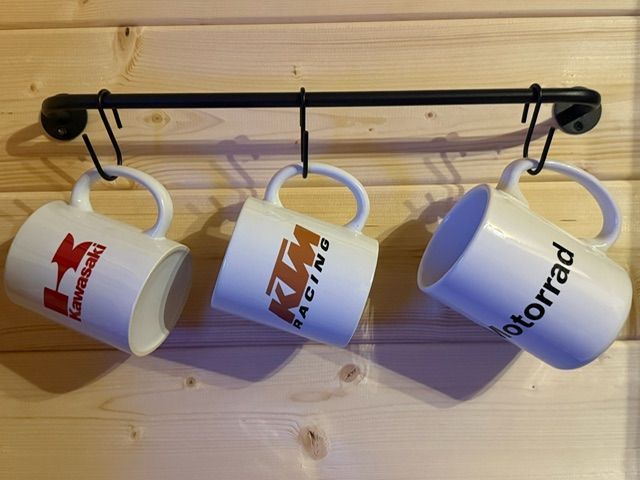 Three white mugs hanging from hooks on a wall rack