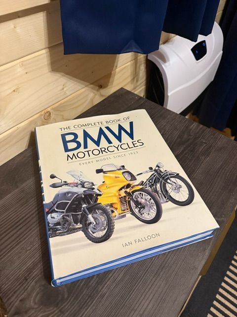 BMW motorcycles book on a dark wooden table beside a white helmet and blue fabric.