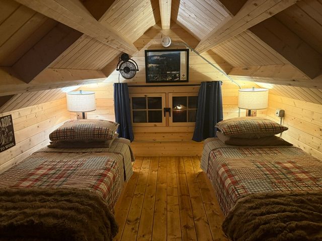 Cozy attic bedroom with two twin beds, warm wood paneling, and matching bedside lamps
