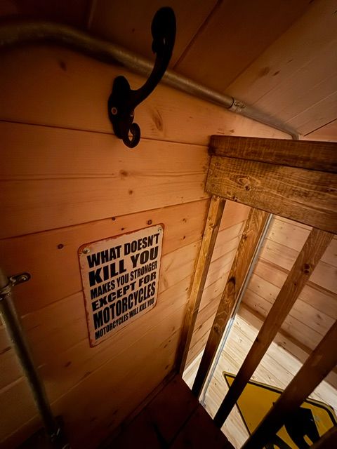 Wooden stairwell with a wall sign reading “What doesn’t kill you makes you stronger” and black metal hooks.