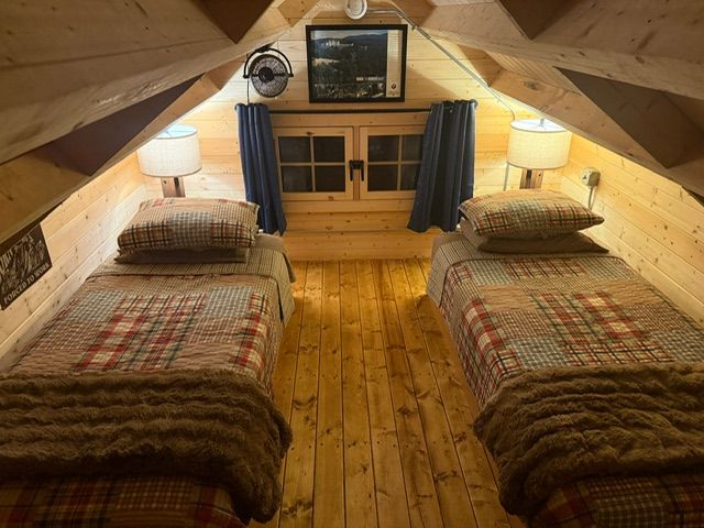 Cozy attic bedroom with two twin beds, warm wood walls, and a small TV at the far end.