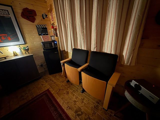 Two black armchairs beside beige curtains in a dimly lit room with warm wood flooring.