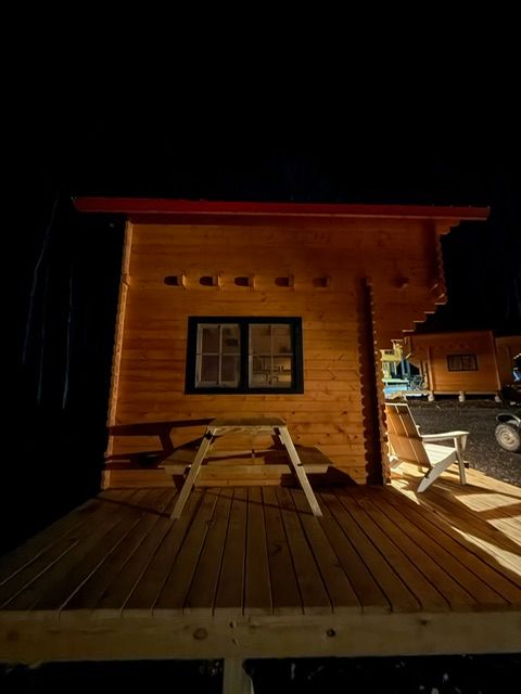 Wooden cabin at night with a picnic table on a lit deck and dark sky.