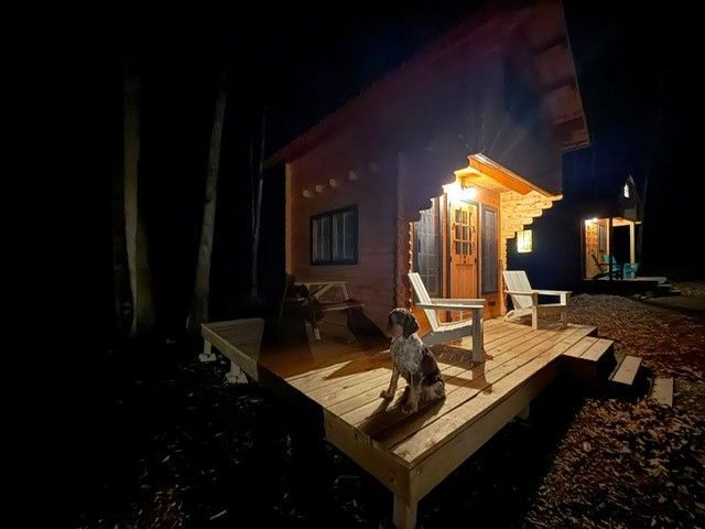 Nighttime cabin porch with warm lights and chairs on a wooden deck overlooking dark water