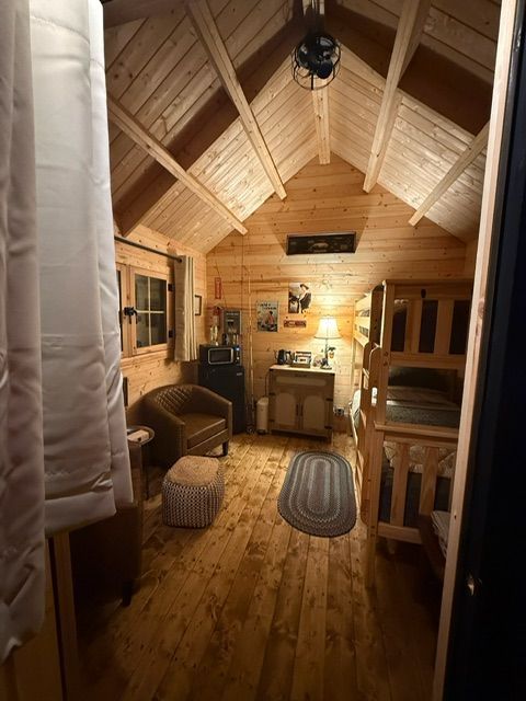 Cozy wooden cabin interior with vaulted ceiling, rug, wicker chair, and warm ambient lighting.