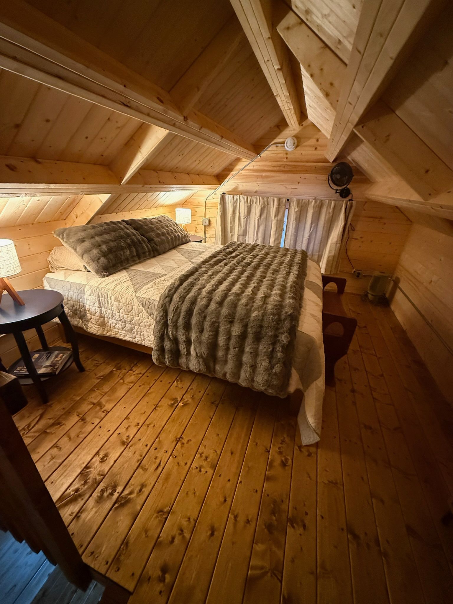 Small attic bedroom with wooden beams, bed, and patterned rug under warm light