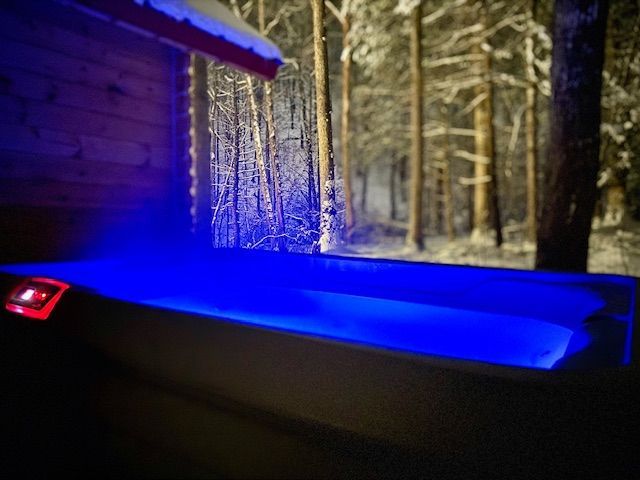 Blue-lit hot tub beside a snowy cabin with frosty trees in the background