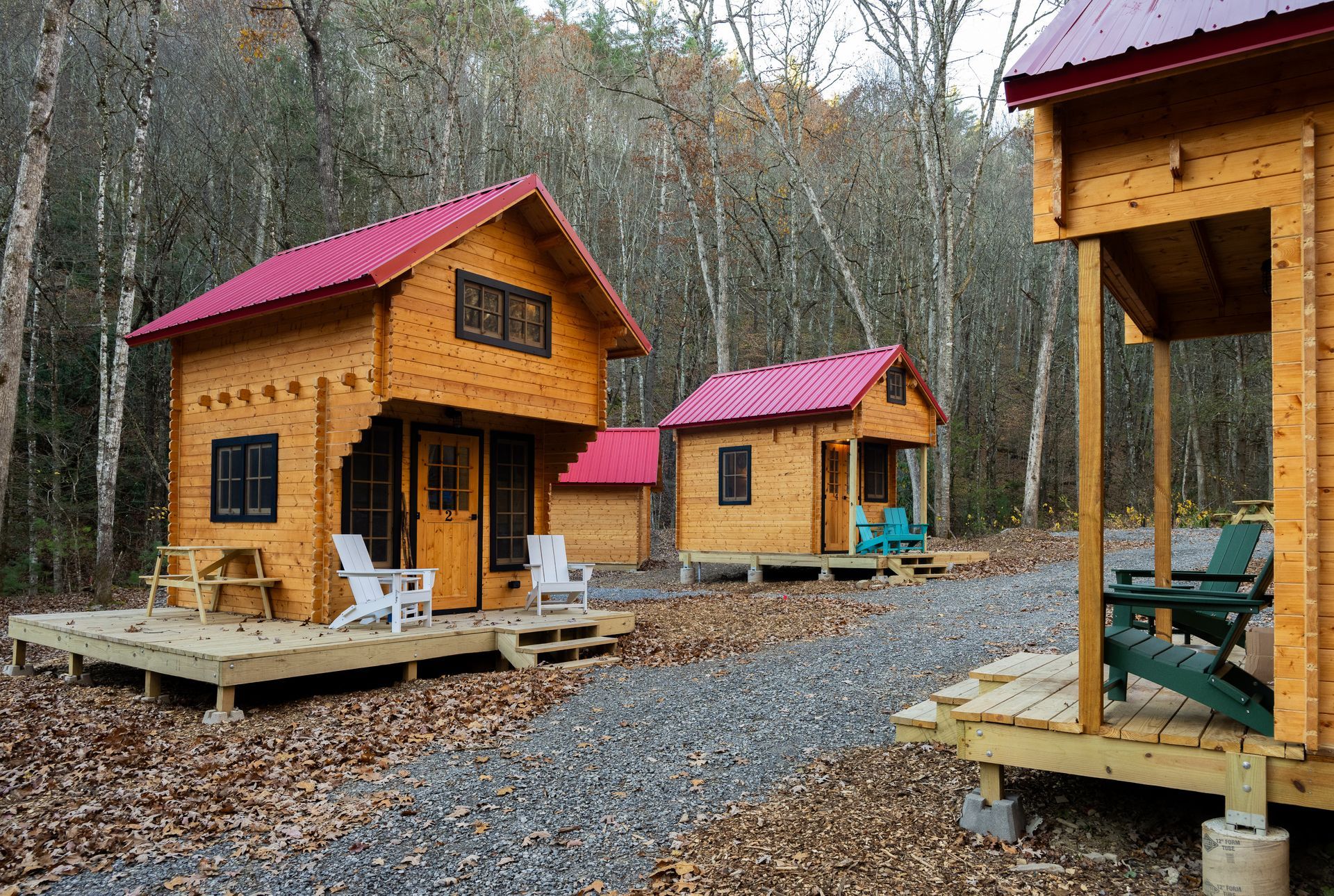 Small wooden cabins with red roofs in a wooded gravel campsite