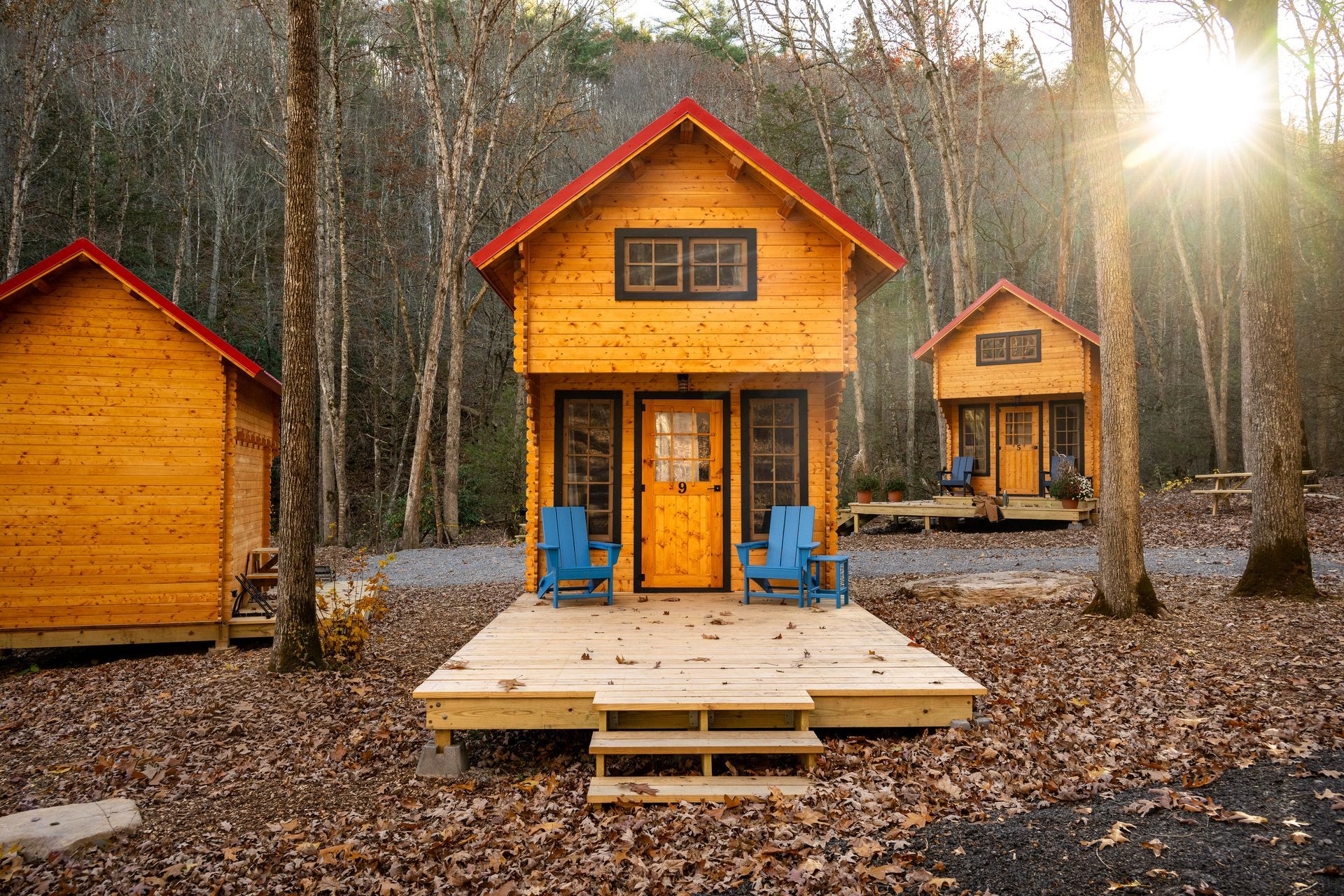 Two orange cabins in a wooded forest, with a small porch and wooden deck in the foreground.