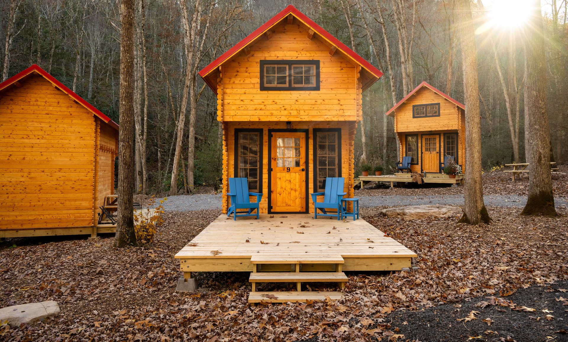 Three orange cabins in a forest clearing, with a small wooden deck and steps in front of the center cabin.