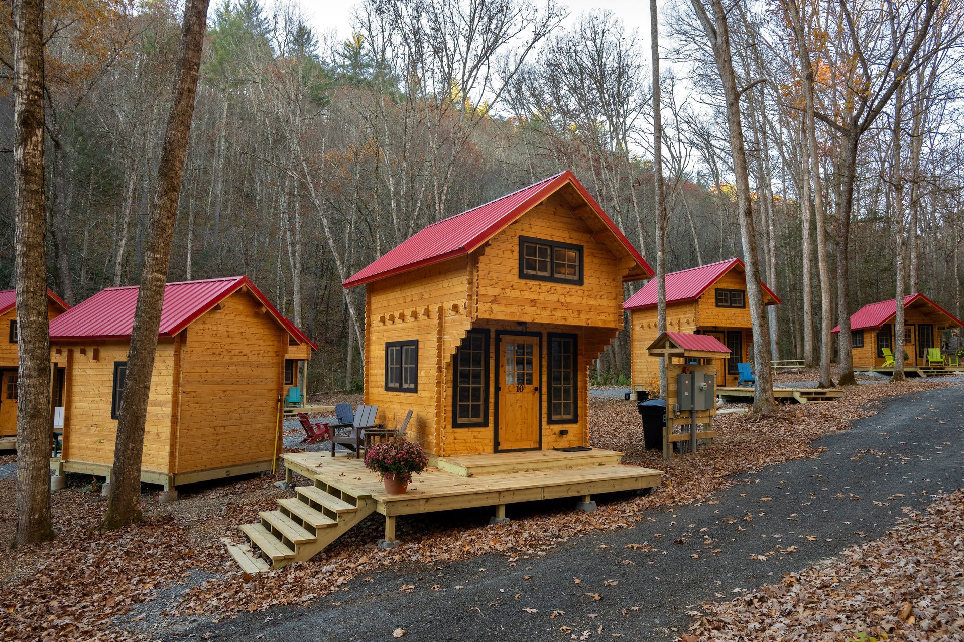 Small wooden cabins with red roofs in a wooded, leaf-covered campground in autumn