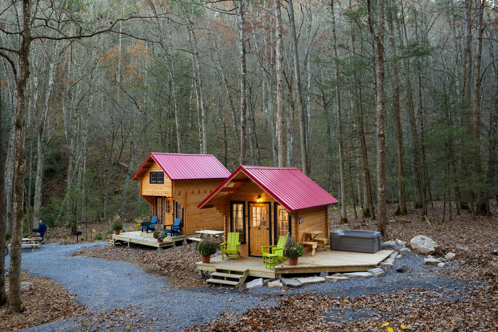 Small wooden cabin with red roof in a leafless forest, lit warmly beside a gravel path