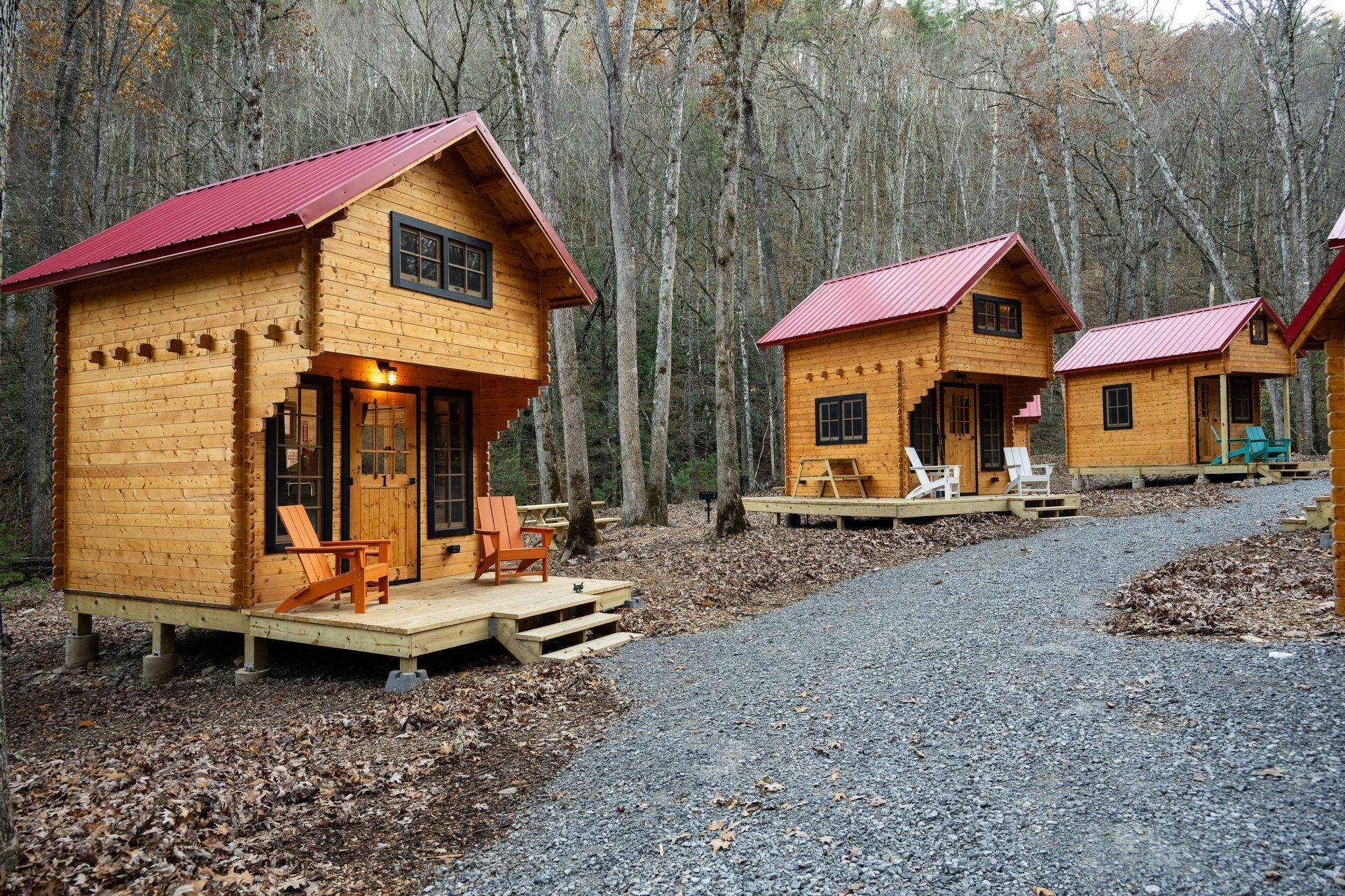 Small wooden cabins with red roofs along a gravel path in a wooded area