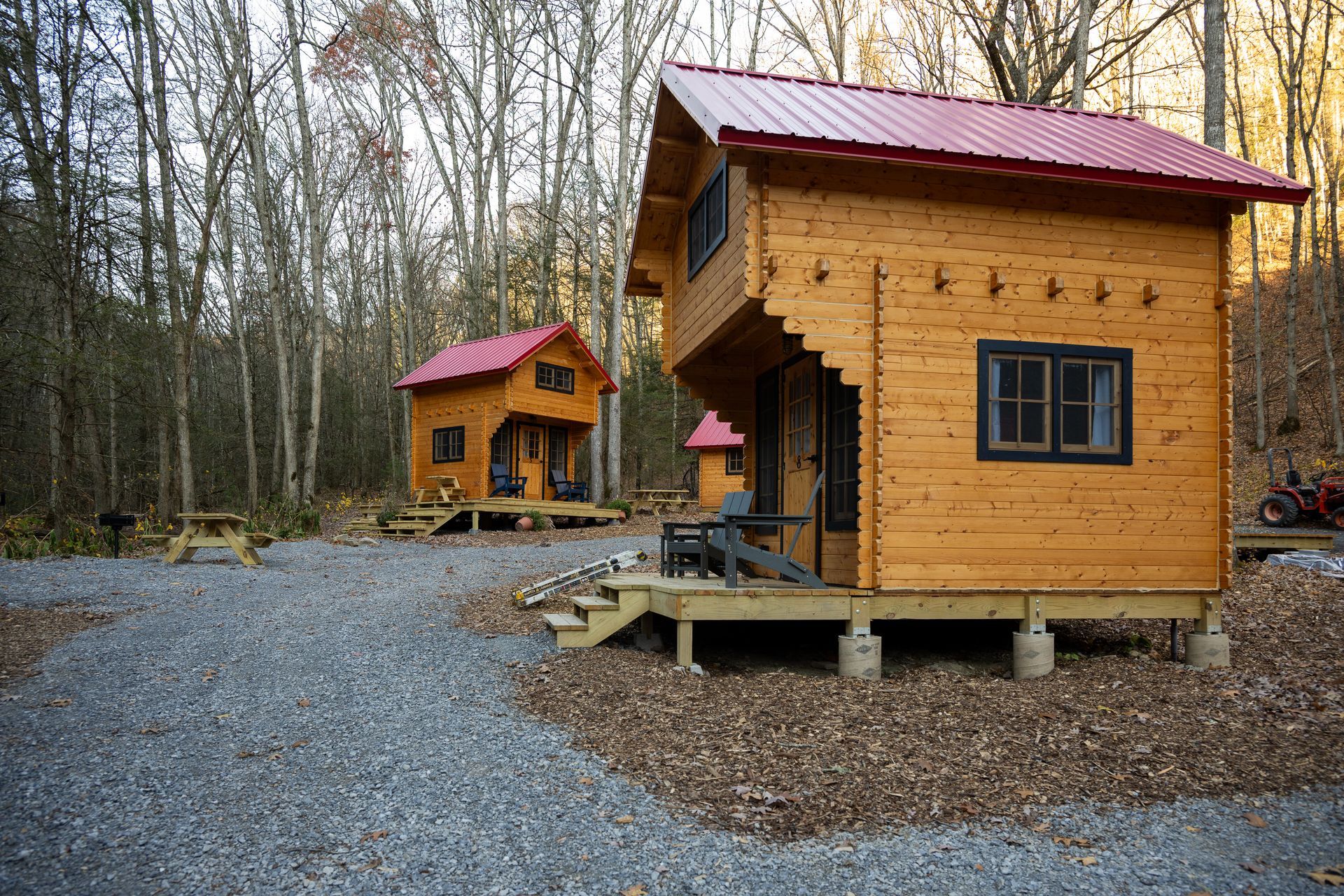 Two small wooden cabins with red roofs on gravel in a wooded campground