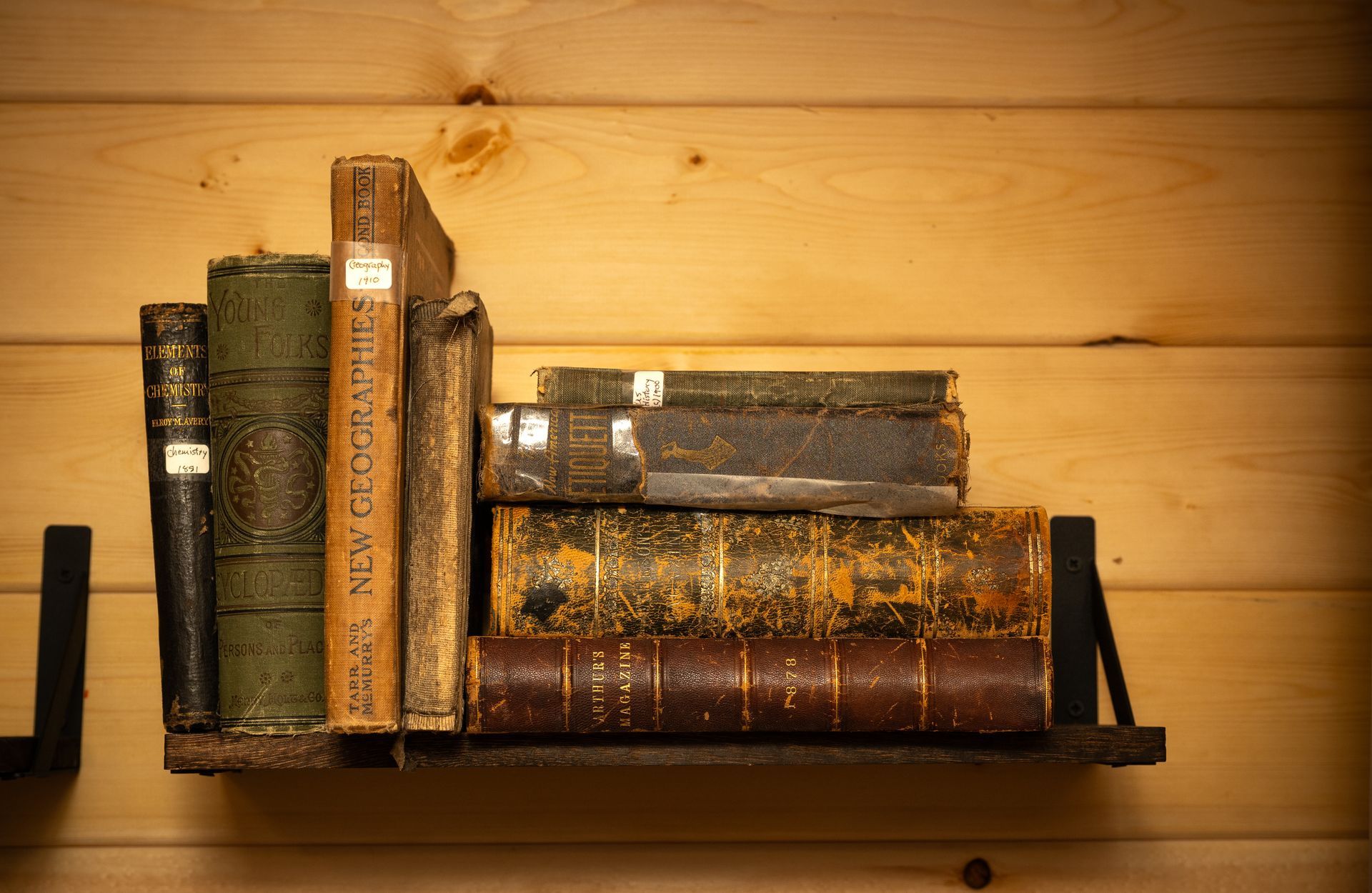 Row of antique books on a black shelf against a warm wooden wall
