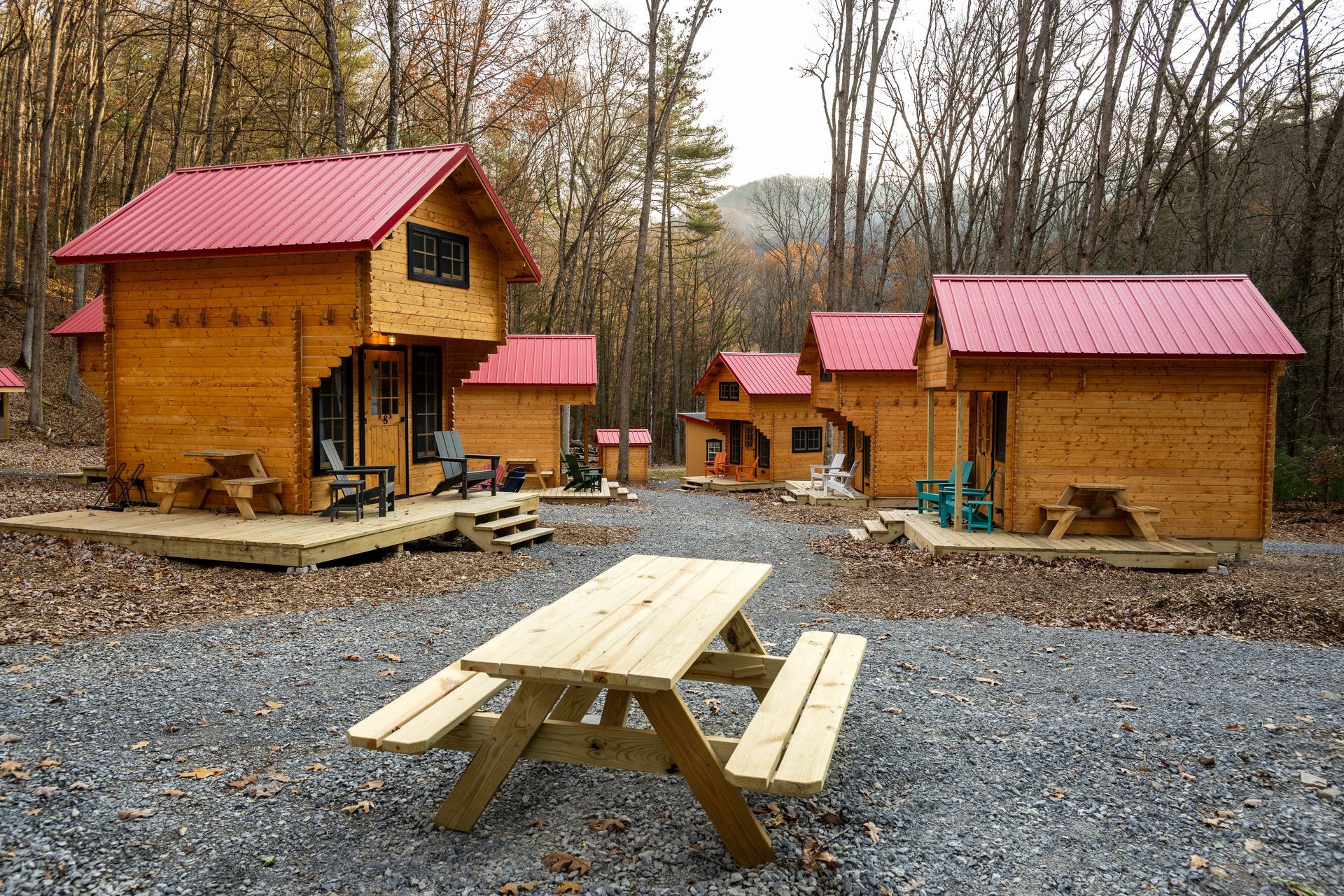 Wooden cabins with red roofs in a wooded park, with a picnic table in the foreground.