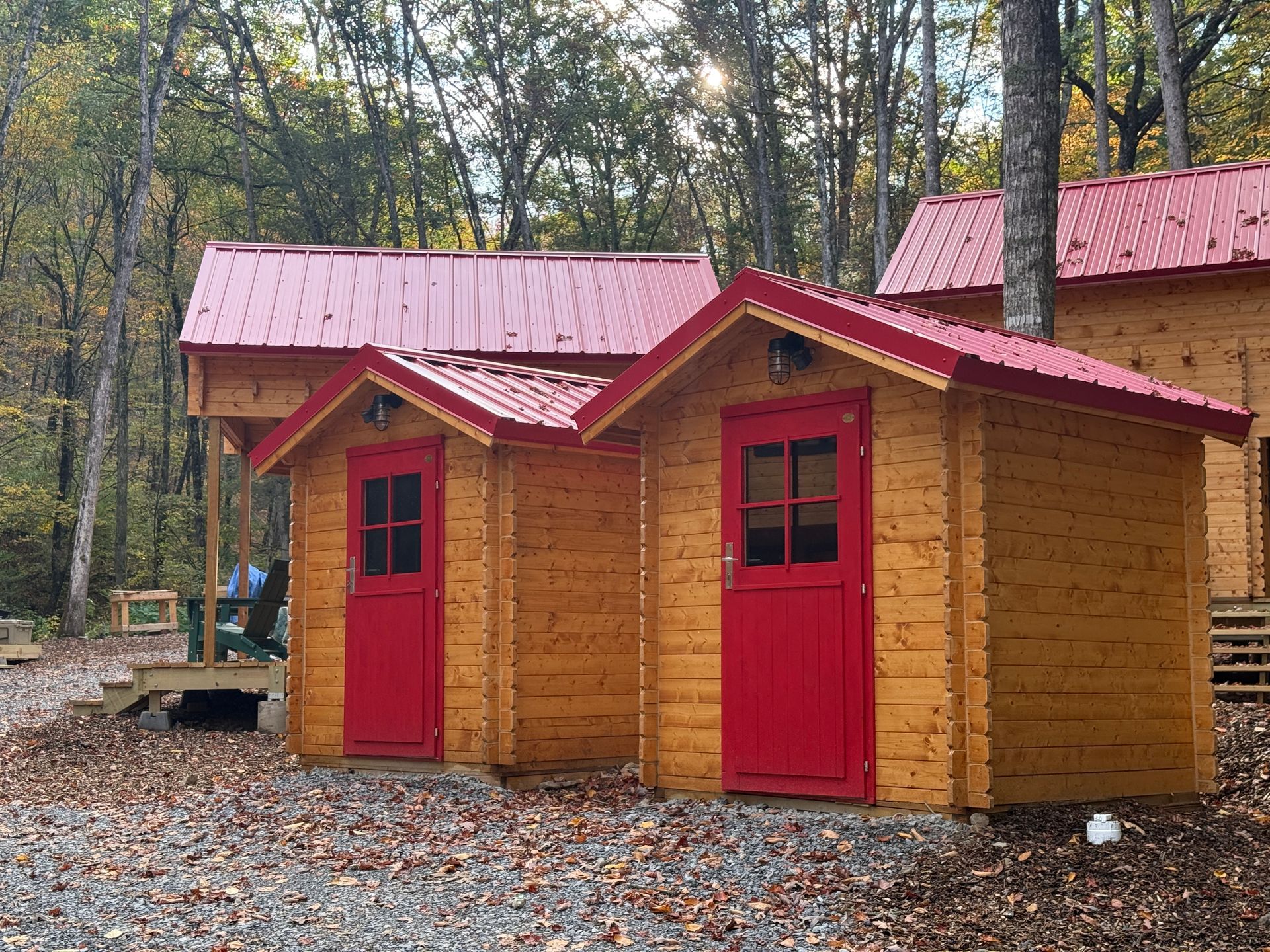 Two small wooden cabins with red roofs and doors in a wooded campground