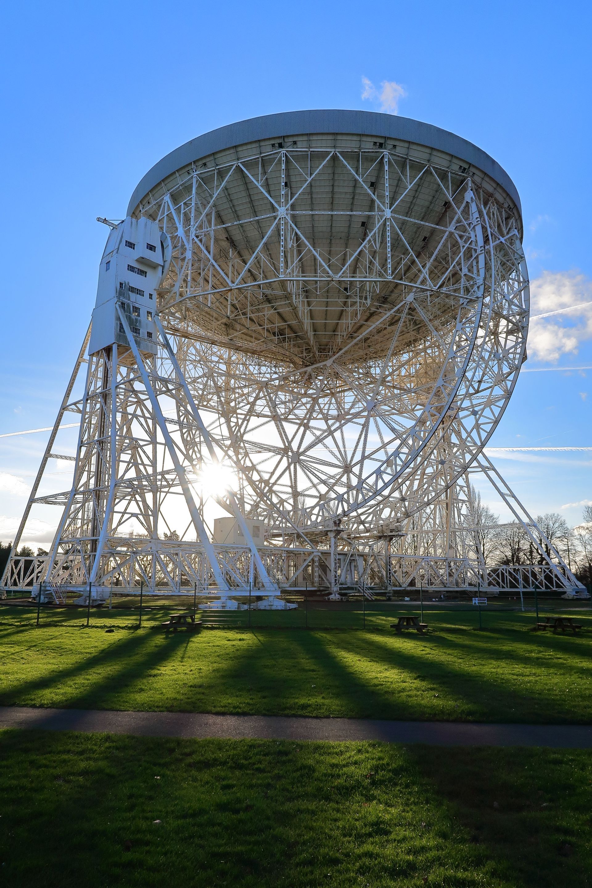 Large white radio telescope dish on a grassy field under a blue sky.