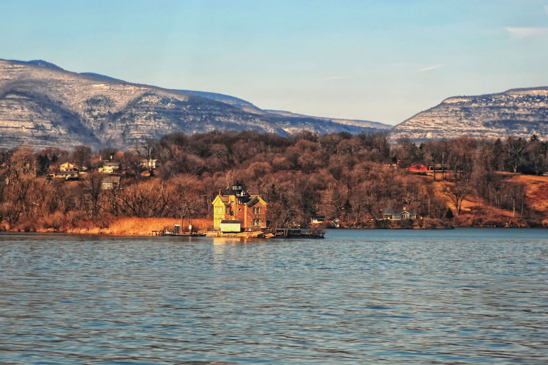 Small yellow house by a lake with mountains and trees in the background at sunset