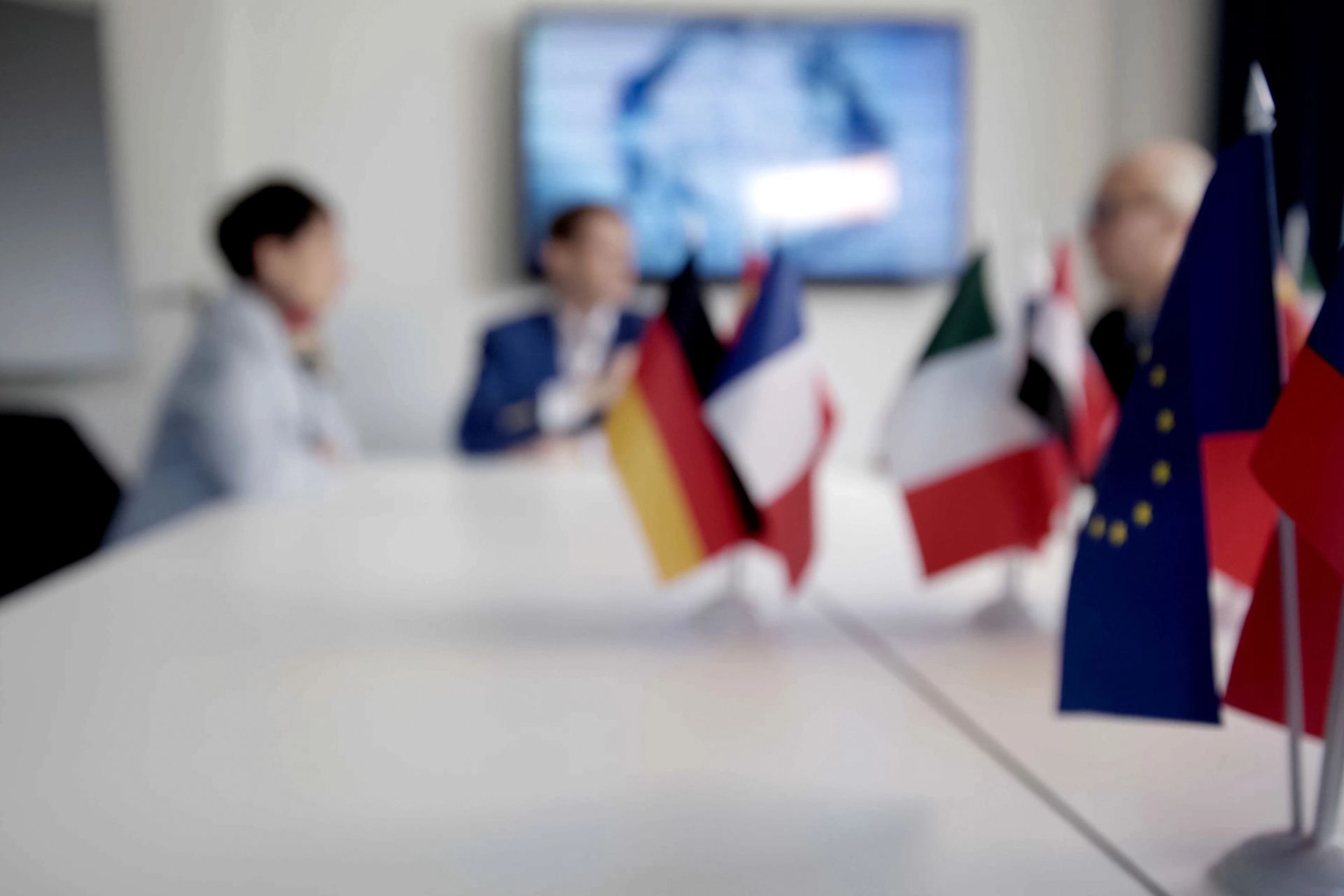 Piccole bandiere su un tavolo da conferenza con persone sfocate che si incontrano sullo sfondo.