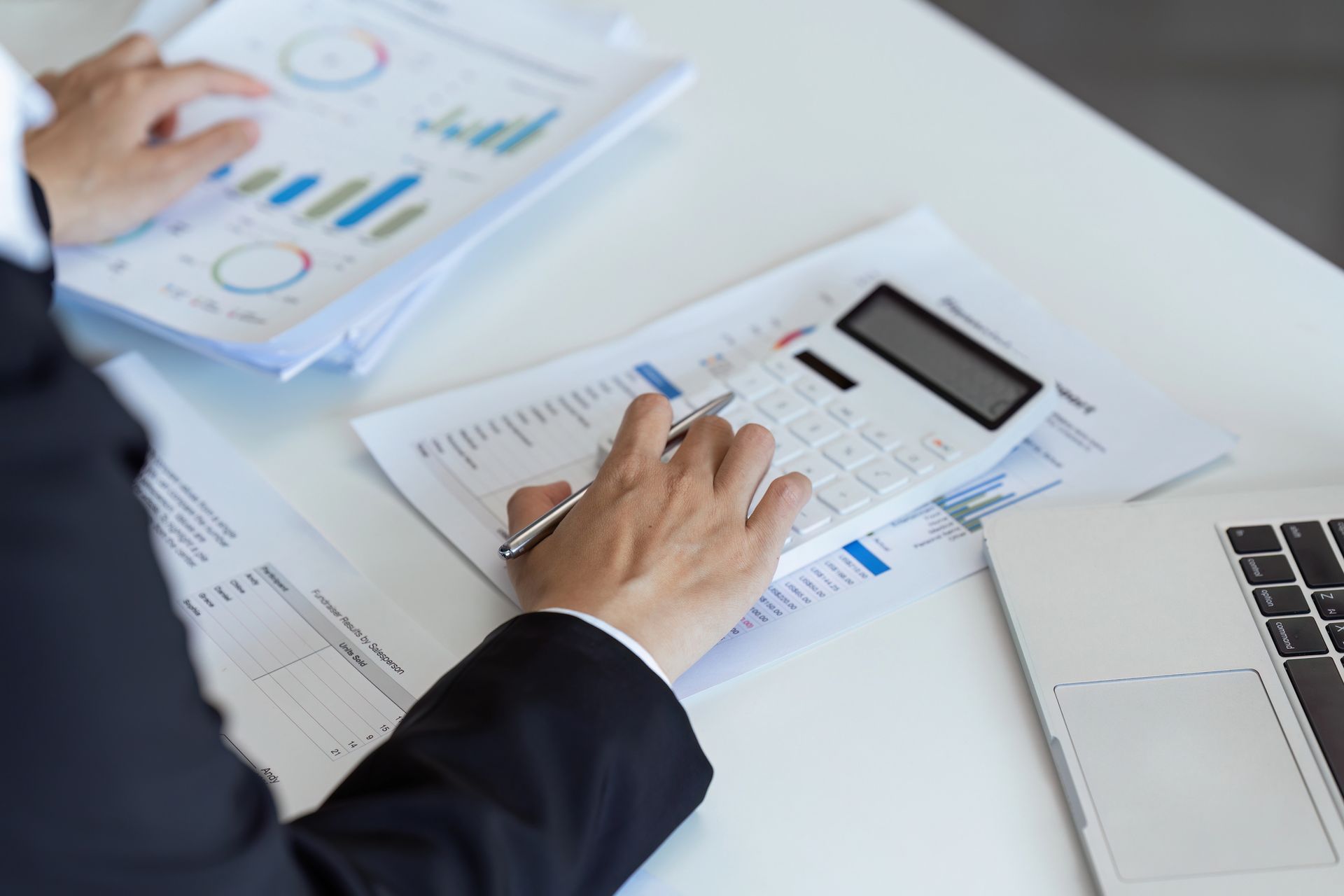 Mani che esaminano grafici e documenti finanziari accanto a un computer portatile in un ambiente d'ufficio.
