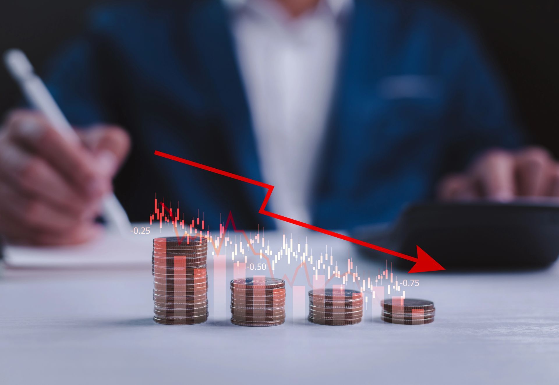 Pile di monete con una freccia rossa rivolta verso il basso, a indicare un calo delle finanze, sullo sfondo di una scrivania.