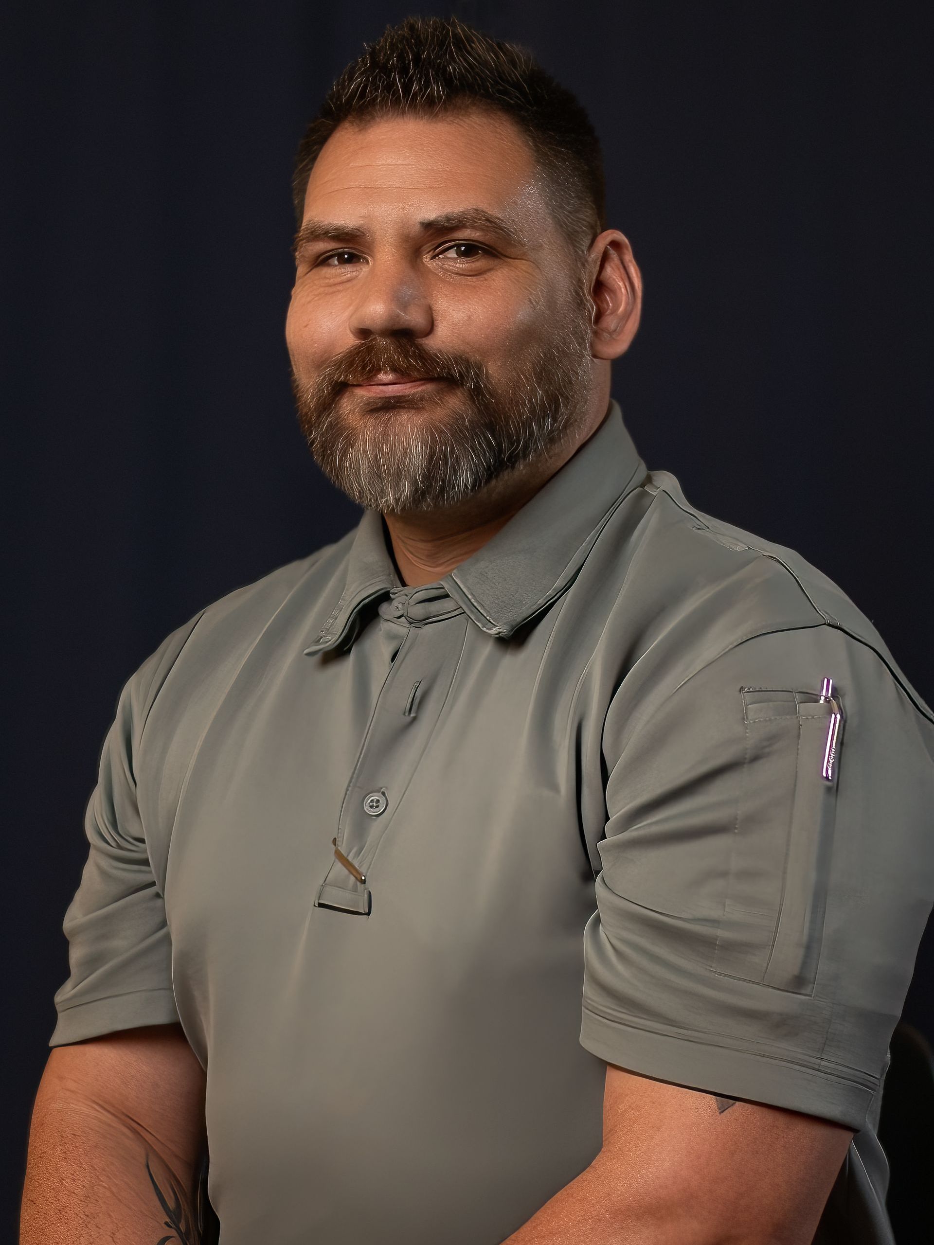 Portrait of a bearded man in a gray polo shirt against a dark background