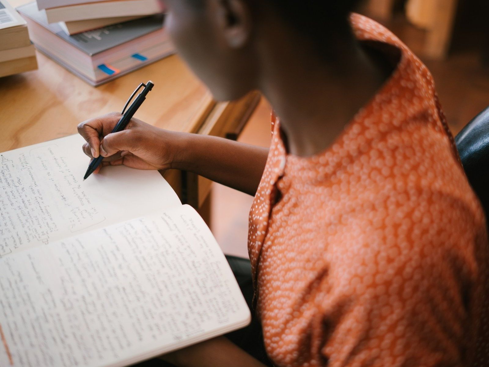 Person writing in a notebook at a desk with books nearby