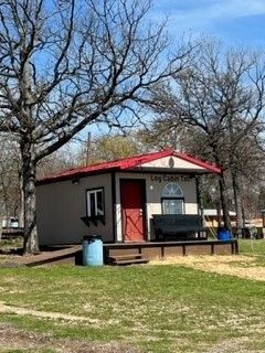 Small beige cabin with a red roof and porch in a grassy park, surrounded by leafless trees.