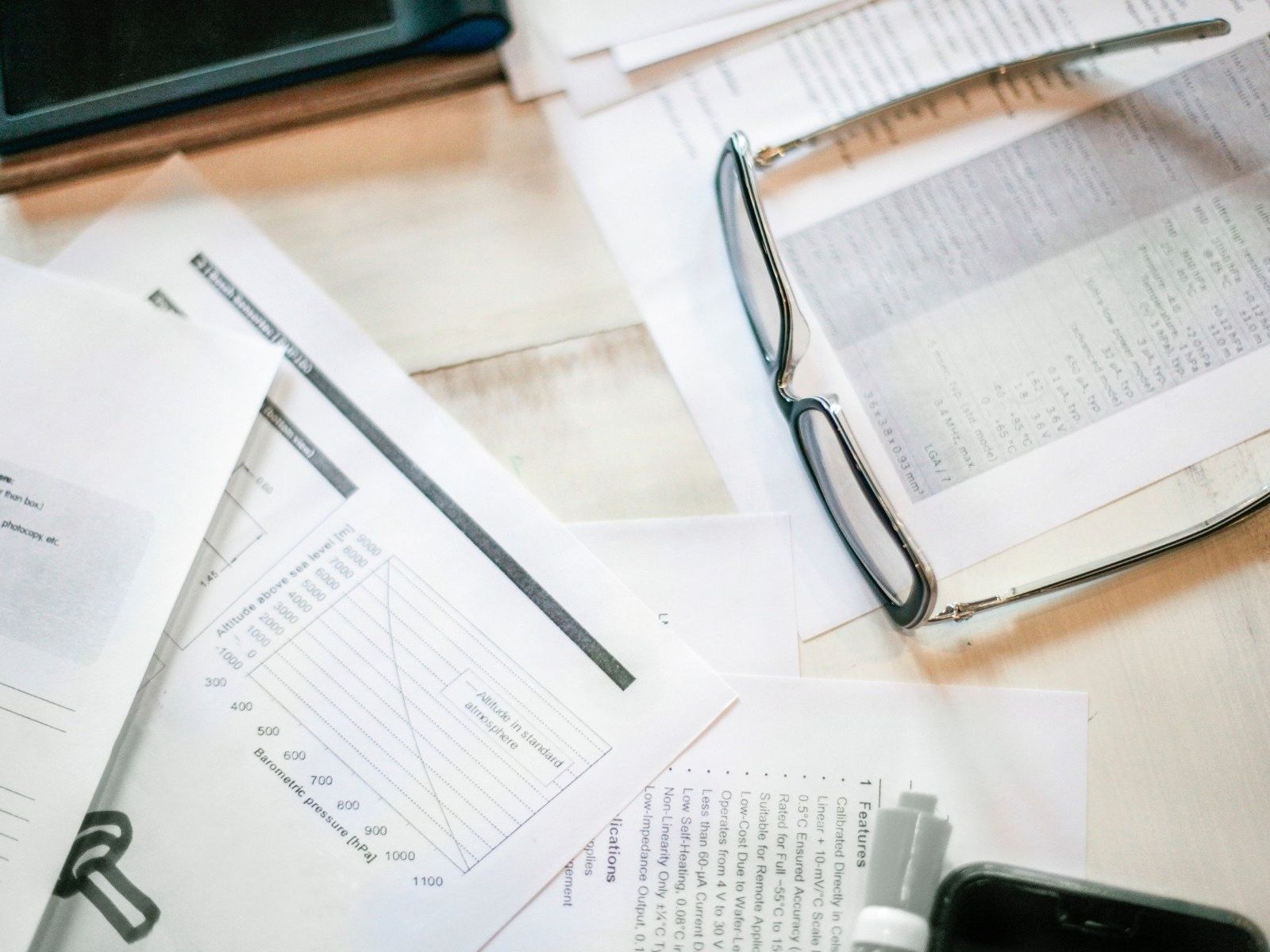 Open documents and a pair of eyeglasses on a desk, viewed from above