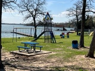 Lakeside playground with slide, picnic table, trees, and a few people near the water