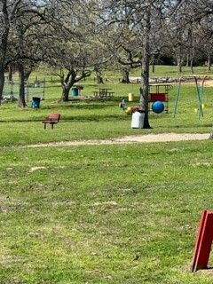 Grassy park with scattered trees, colorful playground equipment, and a dirt path in the foreground