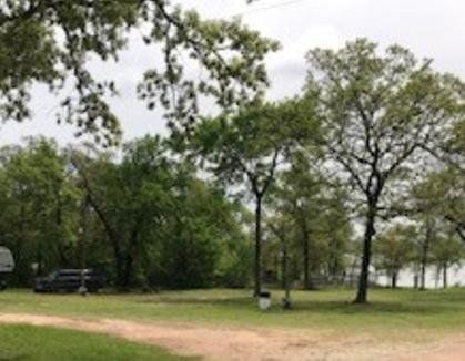 Tree-lined park with a dirt path, grassy field, and a lake in the background