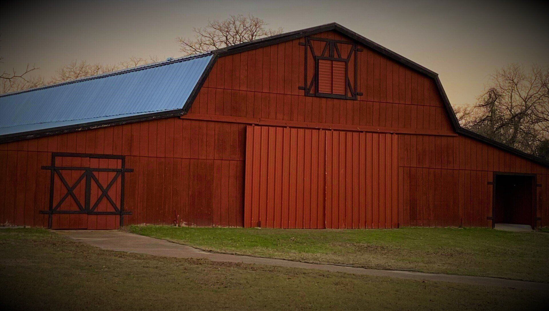 Red barn with blue roof in a grassy field at dusk