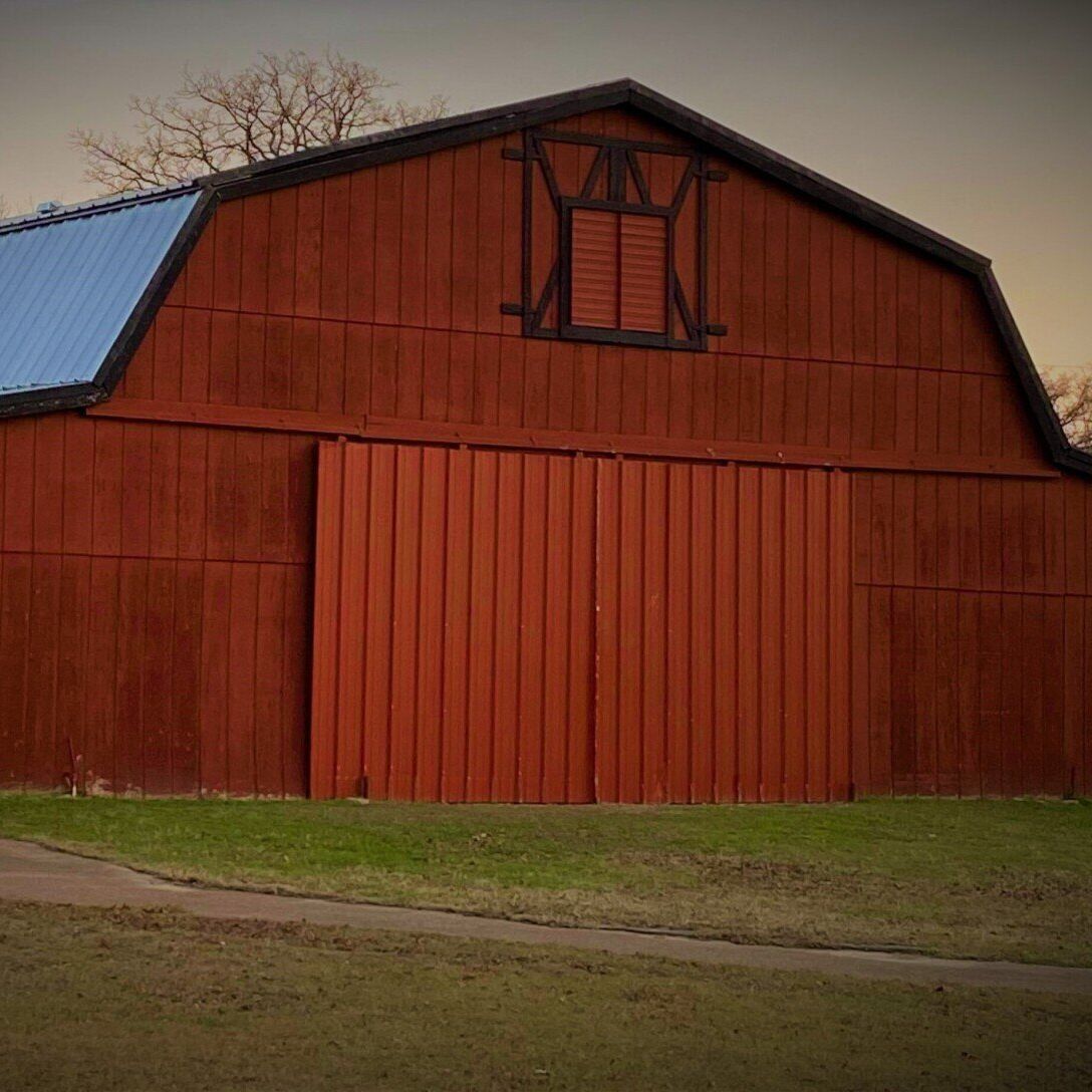 Red barn with large sliding doors on a grassy farm field at dusk
