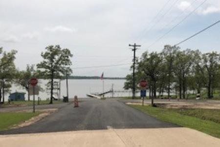 Road leading to a lakeside dock with trees, stop signs, and a utility pole under a cloudy sky