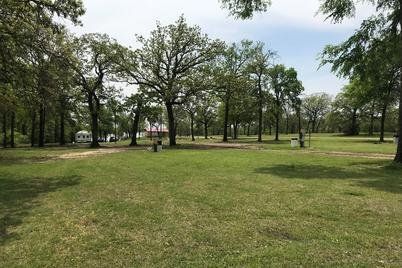 Grassy park with scattered trees and a few people walking near a path