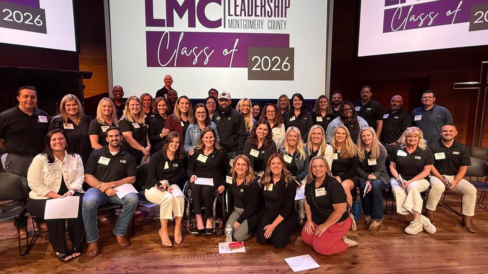 Group of people posing on stage at LMC Leadership Class of 2026 event with banner backdrop
