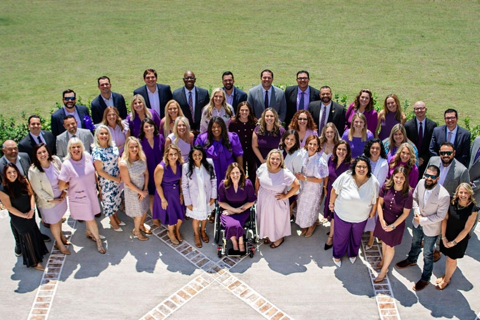 Large group of people in formal and semi-formal attire posing outdoors on a stone patio in front of a lawn