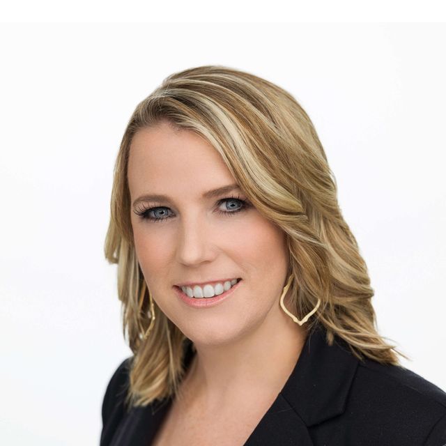 Smiling blonde woman in a black blazer against a white background